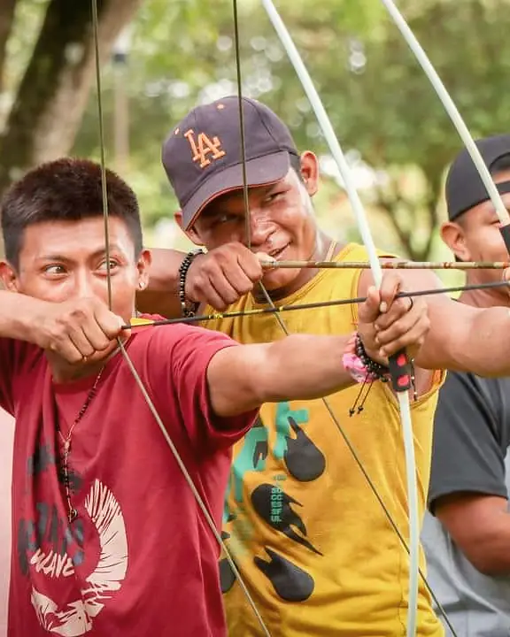 Tres jóvenes concentrados tensan sus arcos al mismo tiempo.
