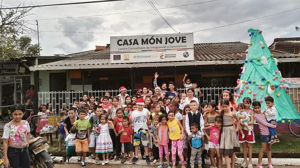 Niñas y niños frente al letrero de Casa Món Jove, junto a un árbol de Navidad hecho a mano.